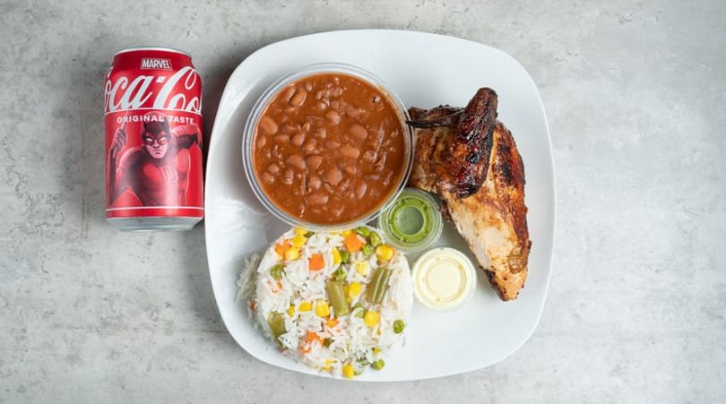Grilled chicken, rice with vegetables, beans, and a Coca-Cola can on a white plate.
